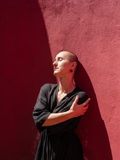 Eine Frau steht vor einer roten Wand und umarmt sich selbst