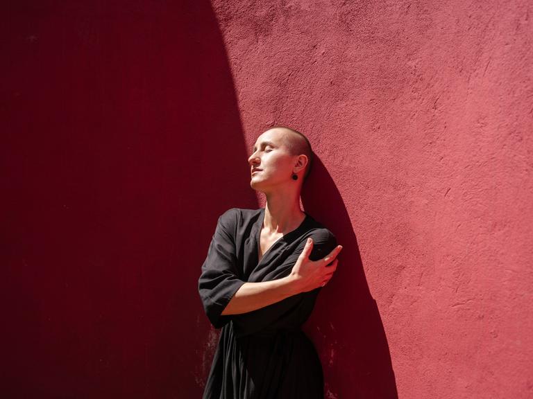 Eine Frau steht vor einer roten Wand und umarmt sich selbst