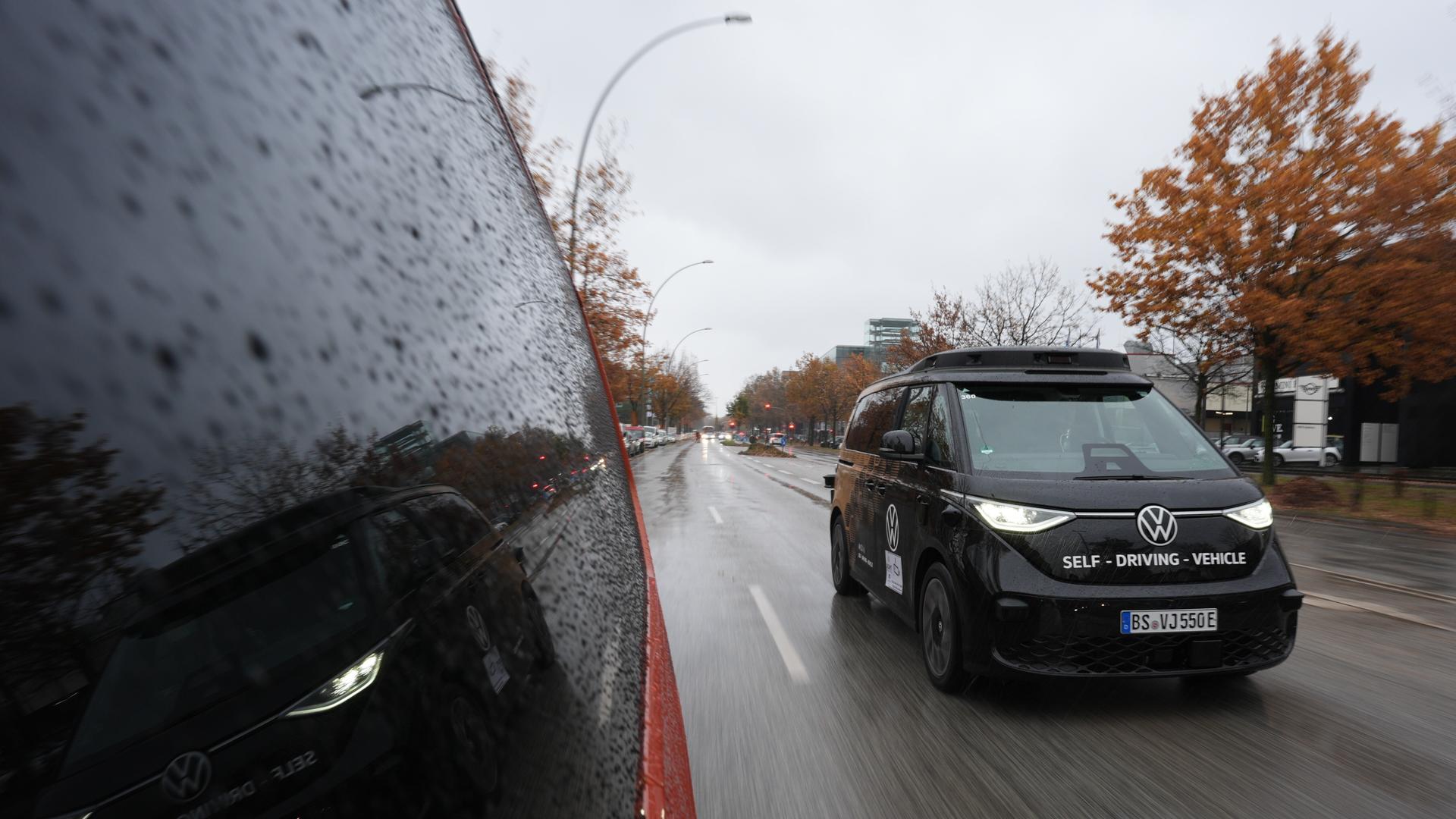 Ein schwarzer Kleinbus der Marke VW fährt auf einer Straße. Vorne auf dem Kleinbus steht "Self Driving Vehicle". Der Kleinbus fährt autonom, also ohne Fahrer. Diese Modelle werden in Hamburg getestet. Ein schwarzer Kleinbus der Marke VW fährt auf einer Straße. Vorne auf dem Kleinbus steht "Self Driving Vehicle". Der Kleinbus fährt autonom, also ohne Fahrer. Diese Modelle werden in Hamburg getestet.