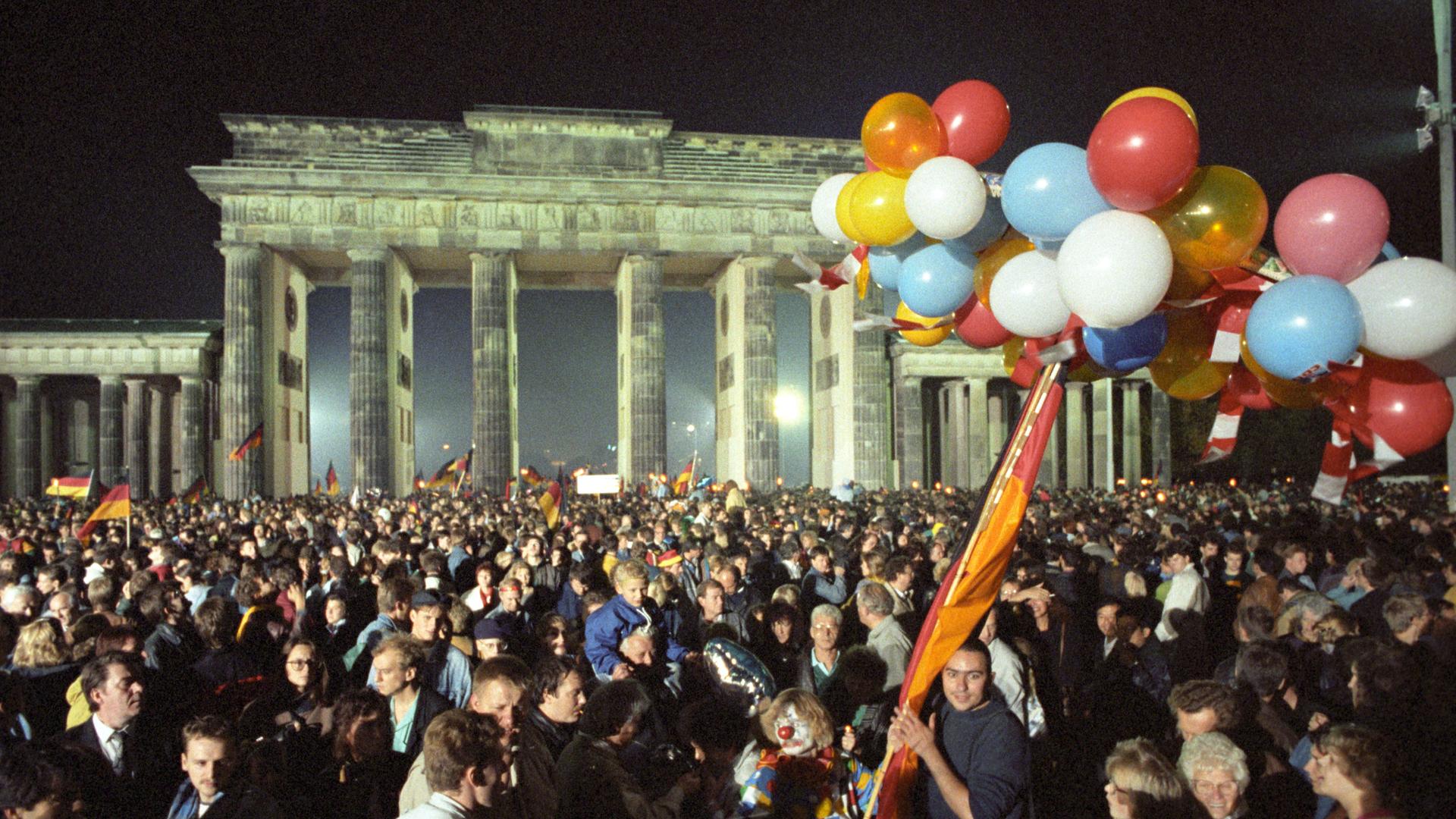 Eine Menschenmange feiert mit Luftballons und Deutschlandfahnen vor dem Brandenburger Tor die Wiedervereinigung in der Nacht auf den 3. Oktober 1990 Eine Menschenmange feiert mit Luftballons und Deutschlandfahnen vor dem Brandenburger Tor die Wiedervereinigung in der Nacht auf den 3. Oktober 1990