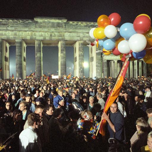 Eine Menschenmange feiert mit Luftballons und Deutschlandfahnen vor dem Brandenburger Tor die Wiedervereinigung in der Nacht auf den 3. Oktober 1990