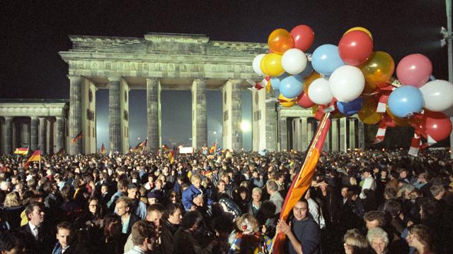 Eine Menschenmange feiert mit Luftballons und Deutschlandfahnen vor dem Brandenburger Tor die Wiedervereinigung in der Nacht auf den 3. Oktober 1990
