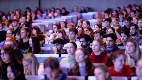 In einem großen Hörsaal sitzen viele Studierende. Sie schauen nach vorne.