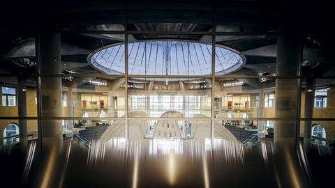 Blick durch eine Glasfront von hinten auf den Bundesadler im Plenum des Bundestages.