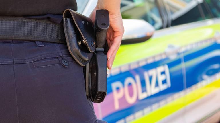 Zu sehen ist eine Polizistin. Sie steht vor einem Streifen-Wagen.