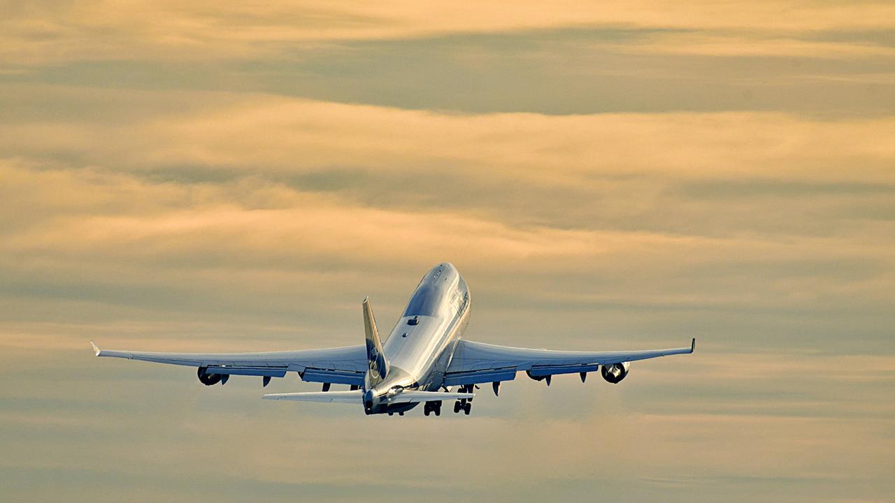 Foto einer startende Boeing 747 der Lufthansa am Frankfurter Flughafen, die vor einem orangefarbenen, bewölkten Abendhimmel aufsteigt.