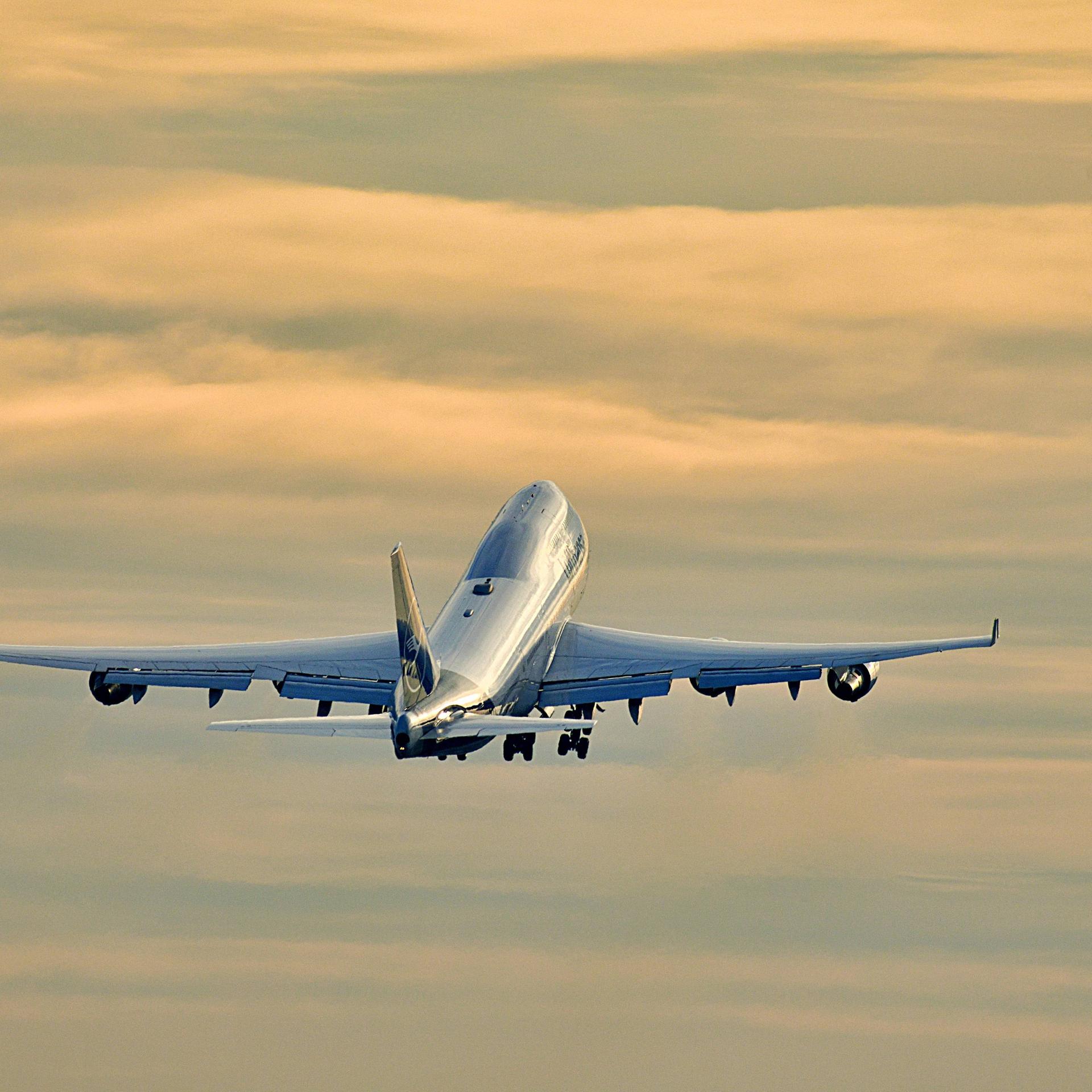 Foto einer startende Boeing 747 der Lufthansa am Frankfurter Flughafen, die vor einem orangefarbenen, bewölkten Abendhimmel aufsteigt.