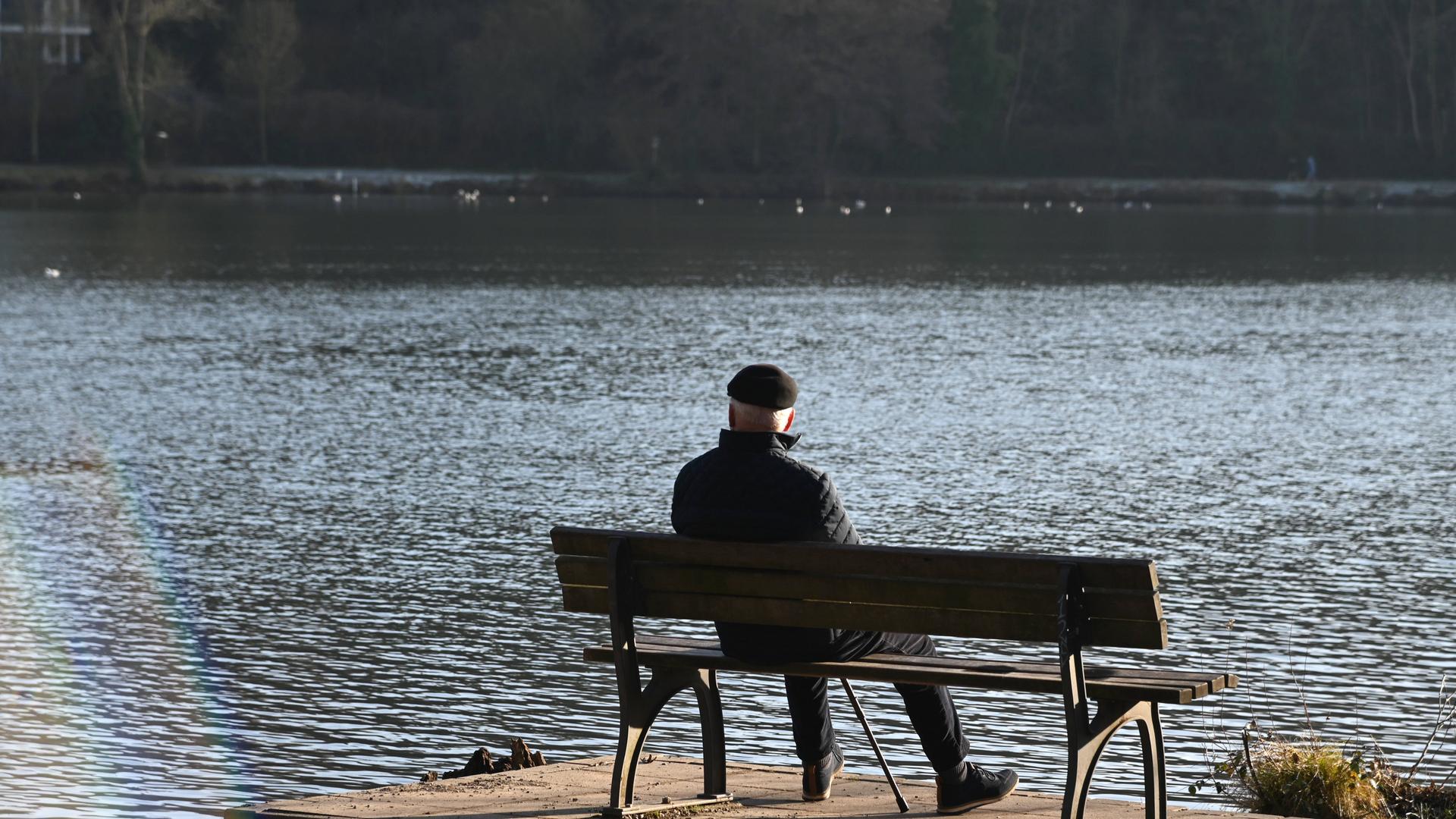 Ein älterer Mann sitzt auf einer Bank und blickt auf einen See Ein älterer Mann sitzt auf einer Bank und blickt auf einen See