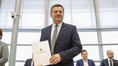 Sven Schulze steht im Landtag in Magdeburg. Er hält einen Ordner mit der Aufschrift "Sachsen-Anhalt" in den Händen.