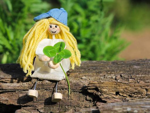 Eine kleine Puppe sitzt mit einem Kleeblatt auf einem Ast