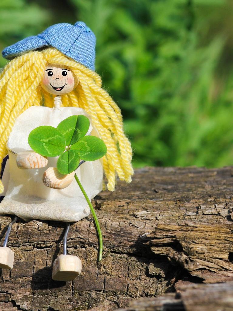 Eine kleine Puppe sitzt mit einem Kleeblatt auf einem Ast