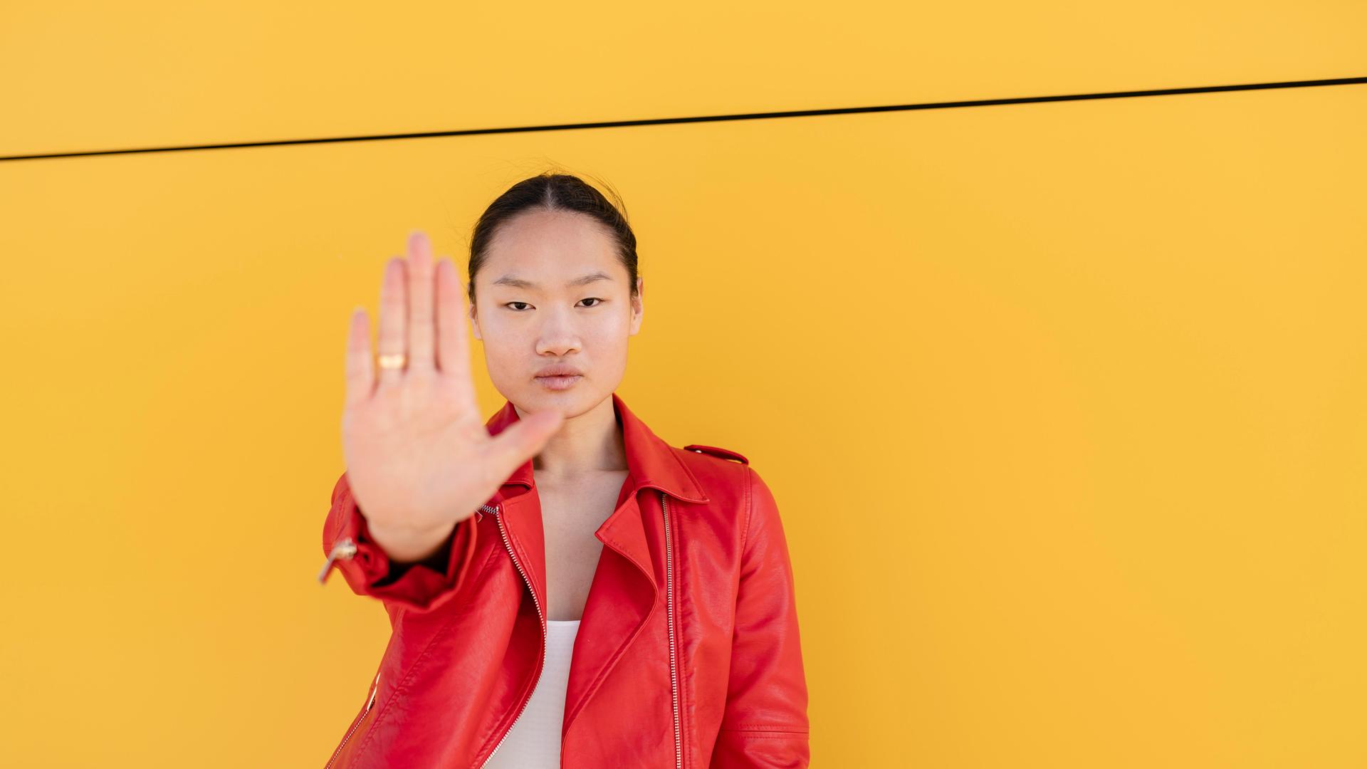 Junge Frau macht vor einer gelben Wand mit der Hand eine Stoppgeste. (Symbolbild zu Femiziden) Junge Frau macht vor einer gelben Wand mit der Hand eine Stoppgeste. (Symbolbild zu Femiziden)