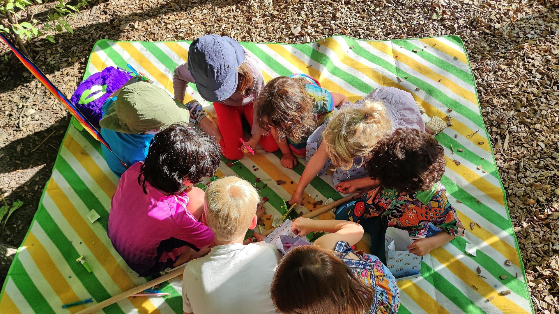 Berlin, Deutschland: Kinder sitzen bei einer Geburtstagsfeier auf einer Decke und beschäftigen sich mit Süßigkeiten