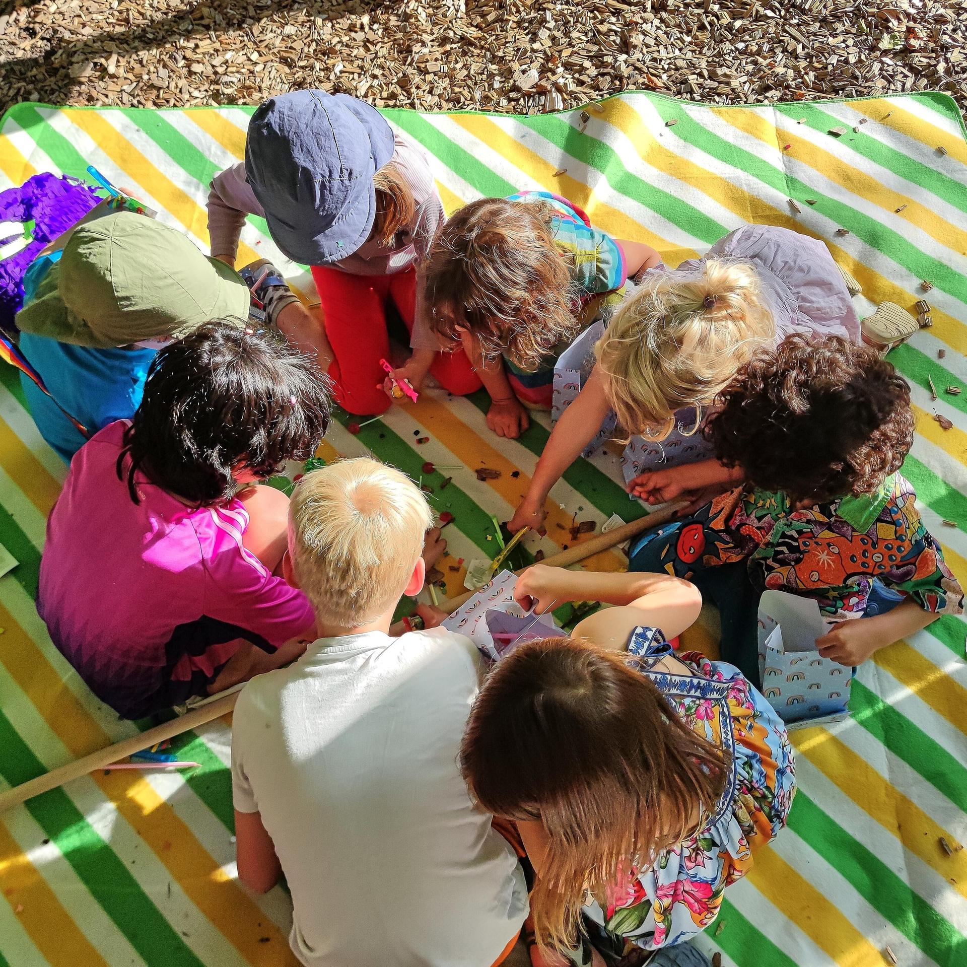 Berlin, Deutschland: Kinder sitzen bei einer Geburtstagsfeier auf einer Decke und beschäftigen sich mit Süßigkeiten