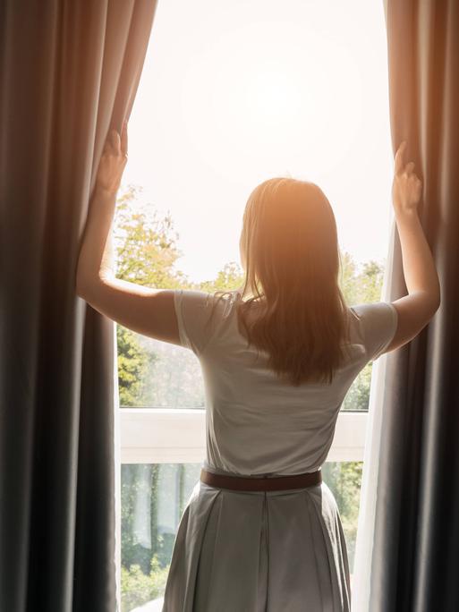 Frau öffnet Vorhänge im Hotelzimmer am sonnigen Morgen. Frau öffnet Vorhänge im Hotelzimmer am sonnigen Morgen.