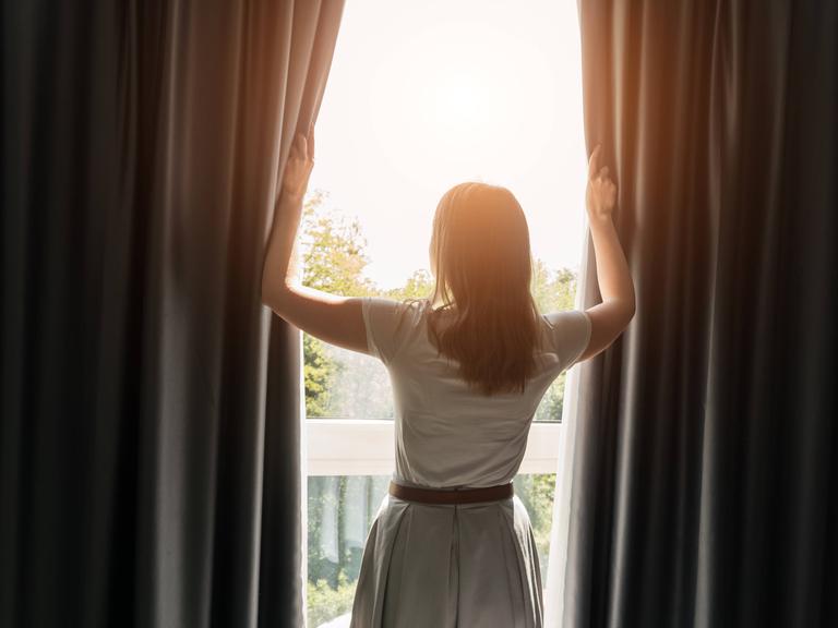 Frau öffnet Vorhänge im Hotelzimmer am sonnigen Morgen. Frau öffnet Vorhänge im Hotelzimmer am sonnigen Morgen.