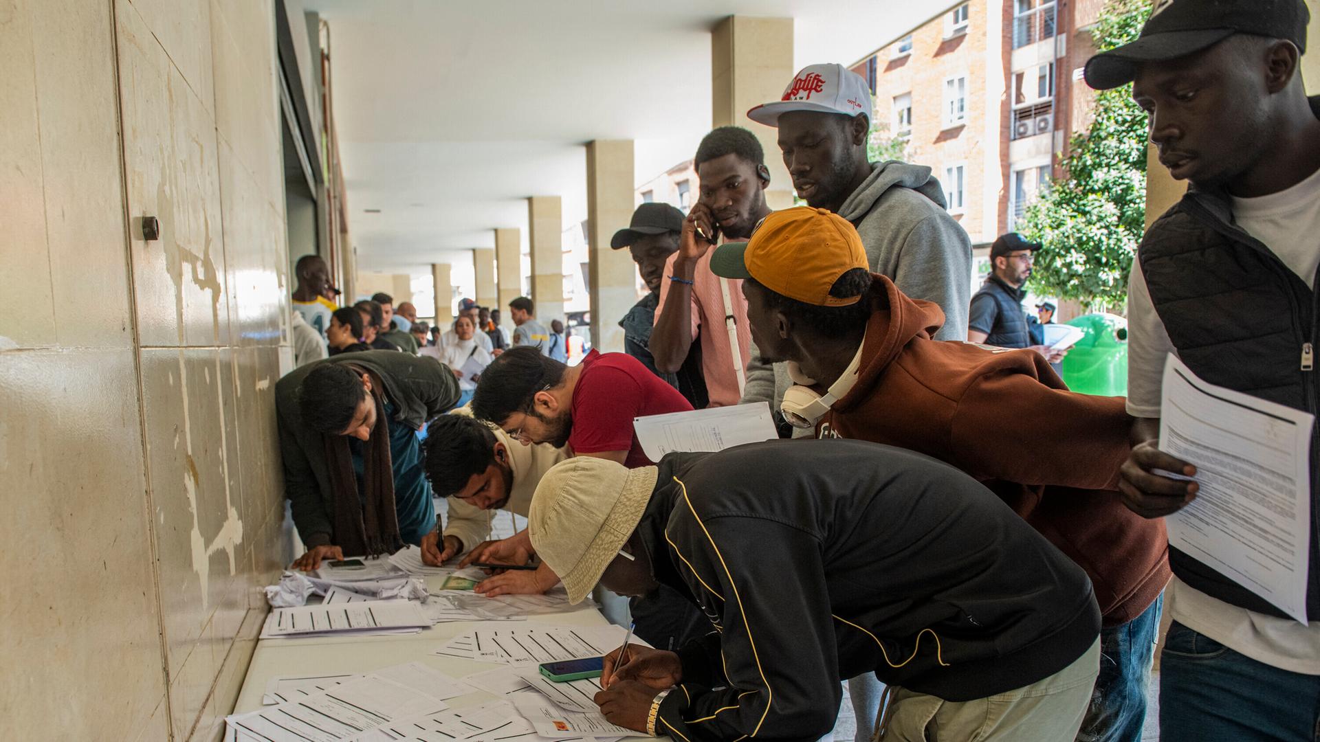 Migranten stehen in einer Behörde Schlange und füllen Formulare aus. Migranten stehen in einer Behörde Schlange und füllen Formulare aus.