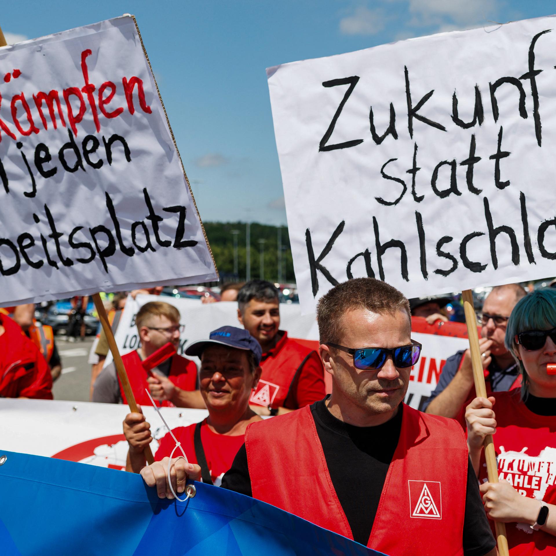 Mitarbeiter von Volkswagen (VW) halten bei einer von der IG Metall organisierten Kundgebung Schilder mit den Aufschriften „Wir kämpfen um jeden Arbeitsplatz“ (links) und „Zukunft statt Kahlschlag“ in die Höhe (9.07.2026, Zwickau)