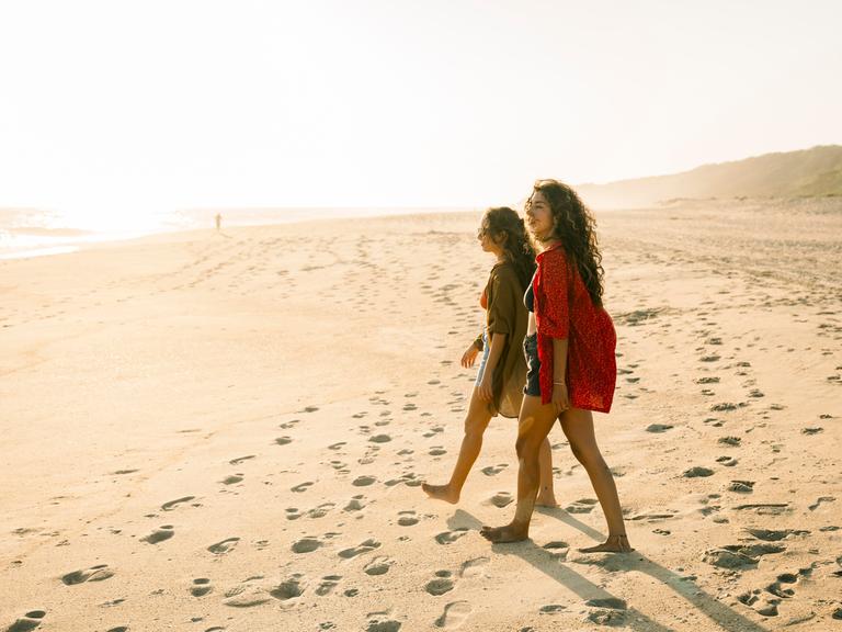 Zwei Menschen, die an einem sonnigen Strand während eines Urlaubs spazieren gehen.