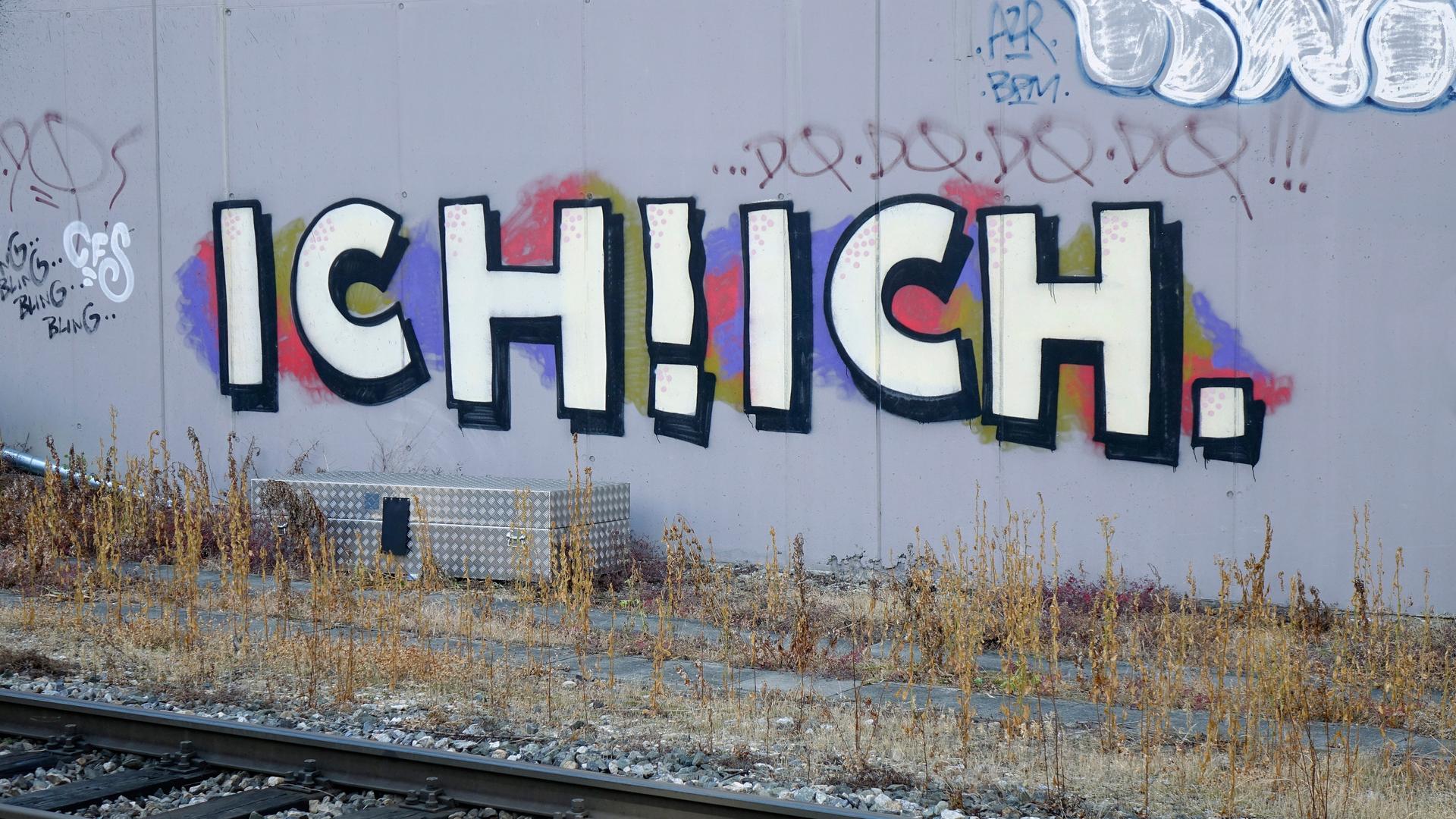 Ich! Ich! steht als Graffiti an einer Wand hinter Bahnschienen. Ich! Ich! steht als Graffiti an einer Wand hinter Bahnschienen.