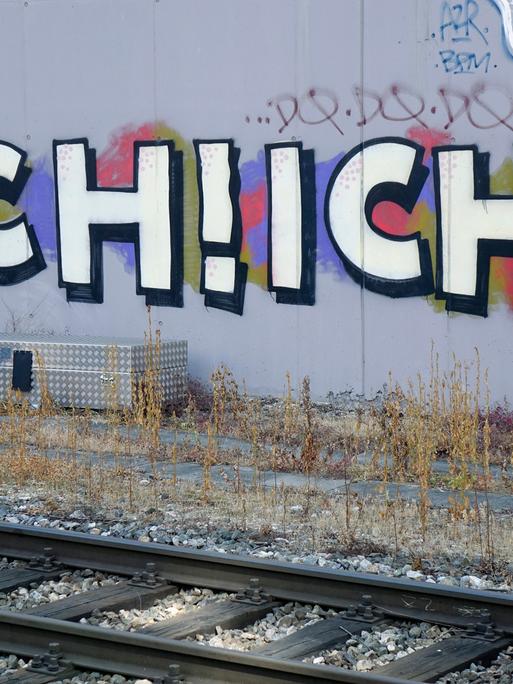 Ich! Ich! steht als Graffiti an einer Wand hinter Bahnschienen.