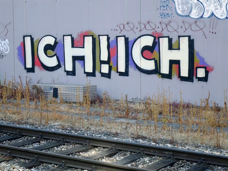 Ich! Ich! steht als Graffiti an einer Wand hinter Bahnschienen.
