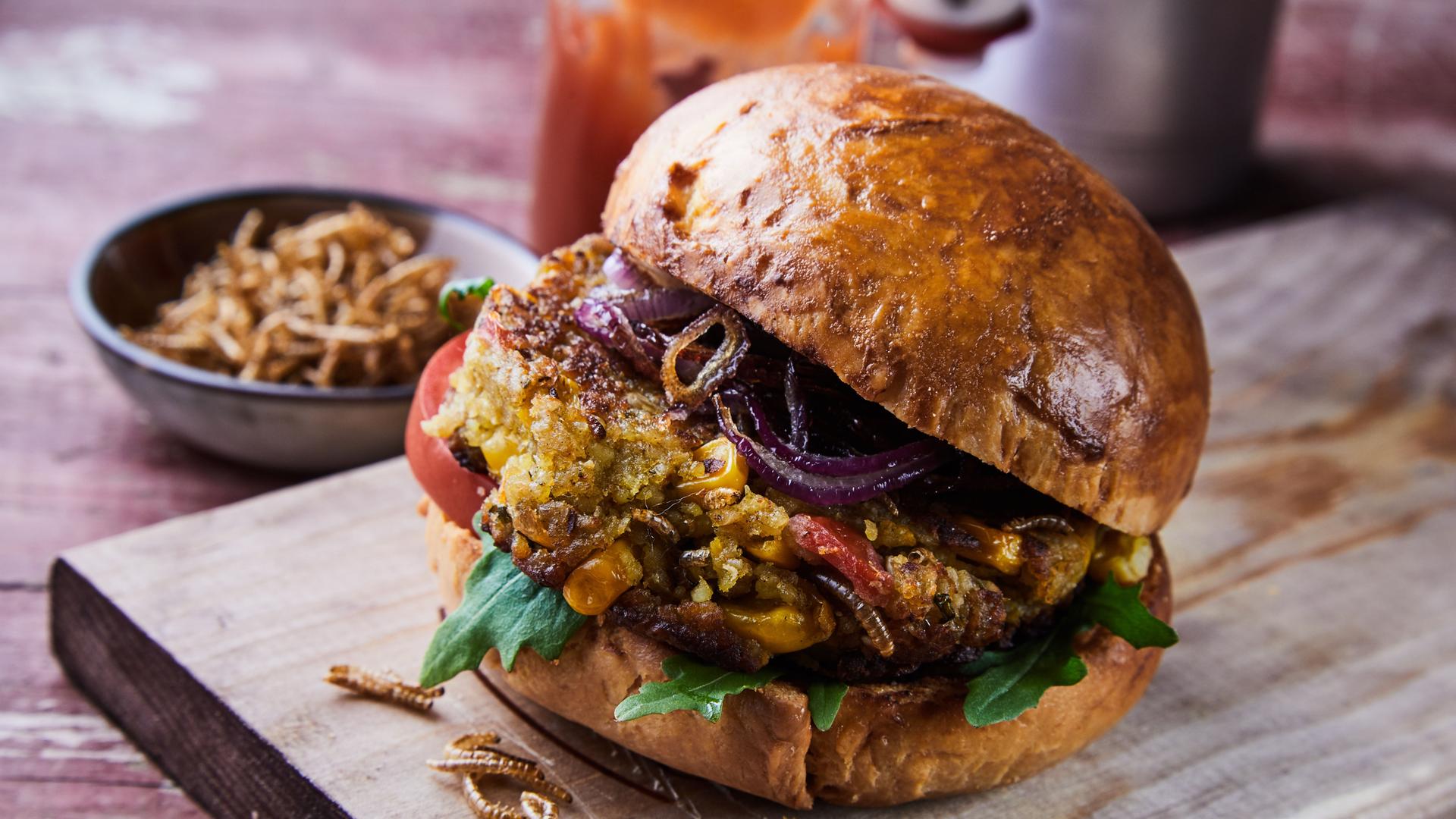 Ein Burger mit frittierten Mehlwürmern, angerichtet auf einem Brett Ein Burger mit frittierten Mehlwürmern, angerichtet auf einem Brett
