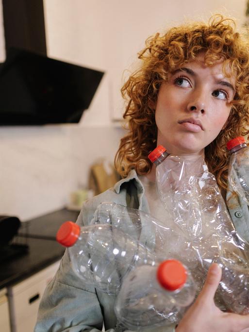 Eine junge Frau steht in einer Küche und hält viele leere Pfandflaschen in den Händen.