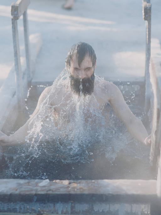 Person mit schwarzen Haarzen und Bart taucht aus dem Eisbad auf Person mit schwarzen Haarzen und Bart taucht aus dem Eisbad auf