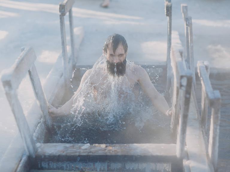 Person mit schwarzen Haarzen und Bart taucht aus dem Eisbad auf Person mit schwarzen Haarzen und Bart taucht aus dem Eisbad auf