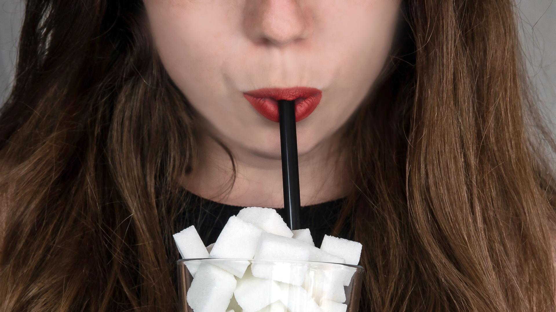 Frau trinkt aus einem Strohhalm, der in einem Glas voller Zuckerwürfel steckt