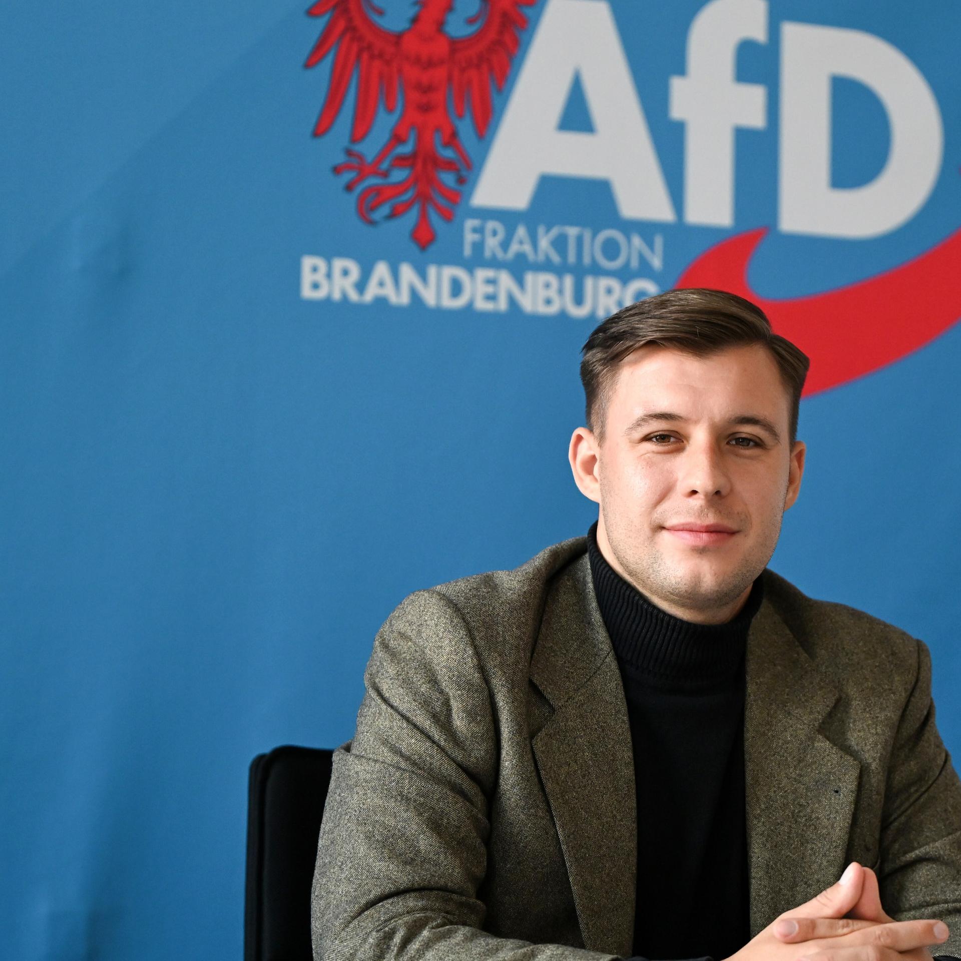 Jean-Pascal Hohm, AfD-Landtagsabgeordneter Brandenburg und Anwärter auf den Vorsitz der neuen AfD-Jugend, sitzt vor einem blauen Banner mit dem Logo der AfD-Brandenburg.