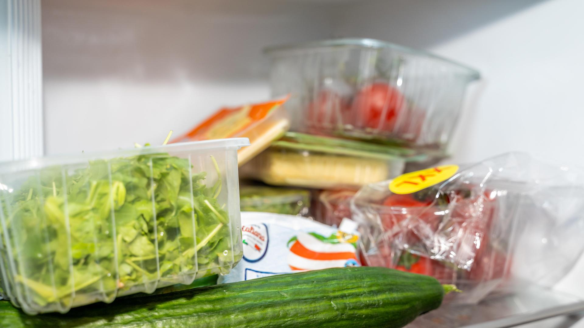 In einem Kühlschrank liegen Gurke, Salat, Tomaten, Käse und weitere Lebensmittel verpackt.