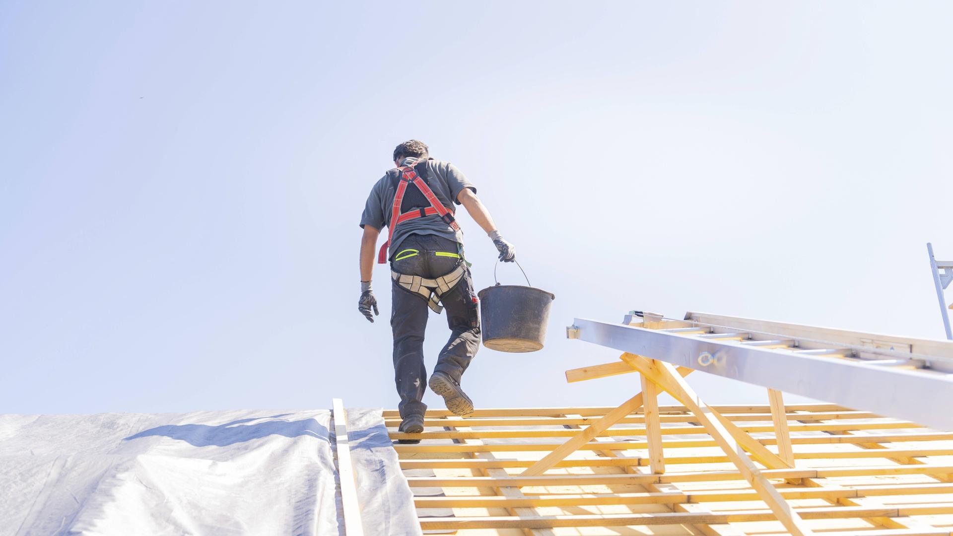 Dachdecker geht mit Eimer in der Hand über ein Dach Dachdecker geht mit Eimer in der Hand über ein Dach
