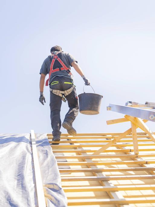 Dachdecker geht mit Eimer in der Hand über ein Dach Dachdecker geht mit Eimer in der Hand über ein Dach