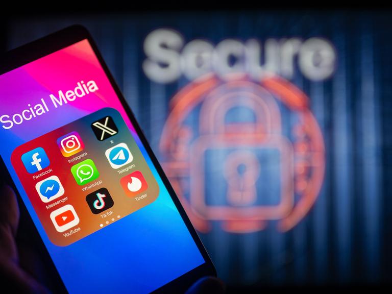 Social-Media-Symbole werden auf einem Smartphone angezeigt, im Hintergrund ist ein Sicherheitsschloss zu sehen.