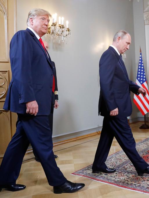 Us-Präsident Trump und Russlands Prösident Putin laufen durch einen Raum, im Hintergrund sieht man die Flaggen von Russland und den USA.