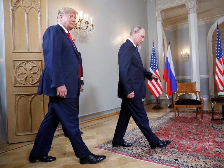 Us-Präsident Trump und Russlands Prösident Putin laufen durch einen Raum, im Hintergrund sieht man die Flaggen von Russland und den USA.