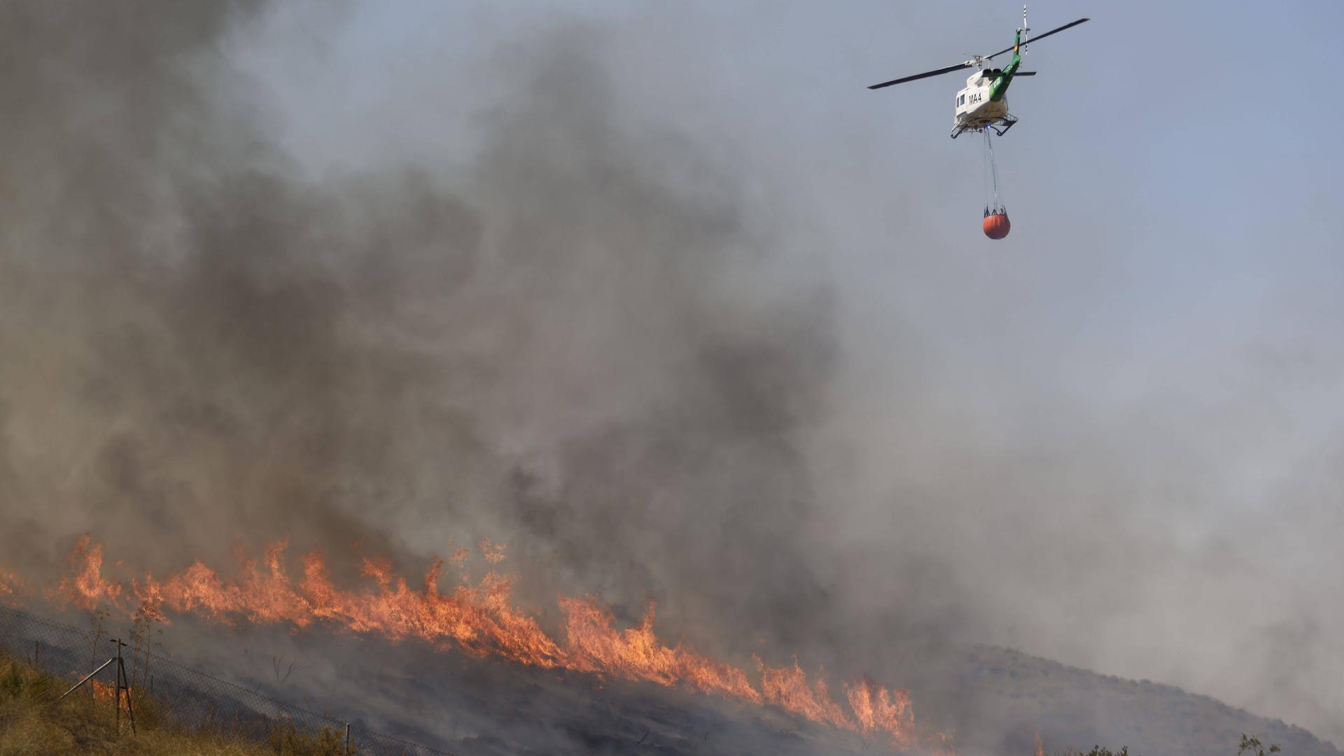 Ein Löschhubschrauber fliegt über einem brennenden Waldgebiet. Ein Löschhubschrauber fliegt über einem brennenden Waldgebiet.