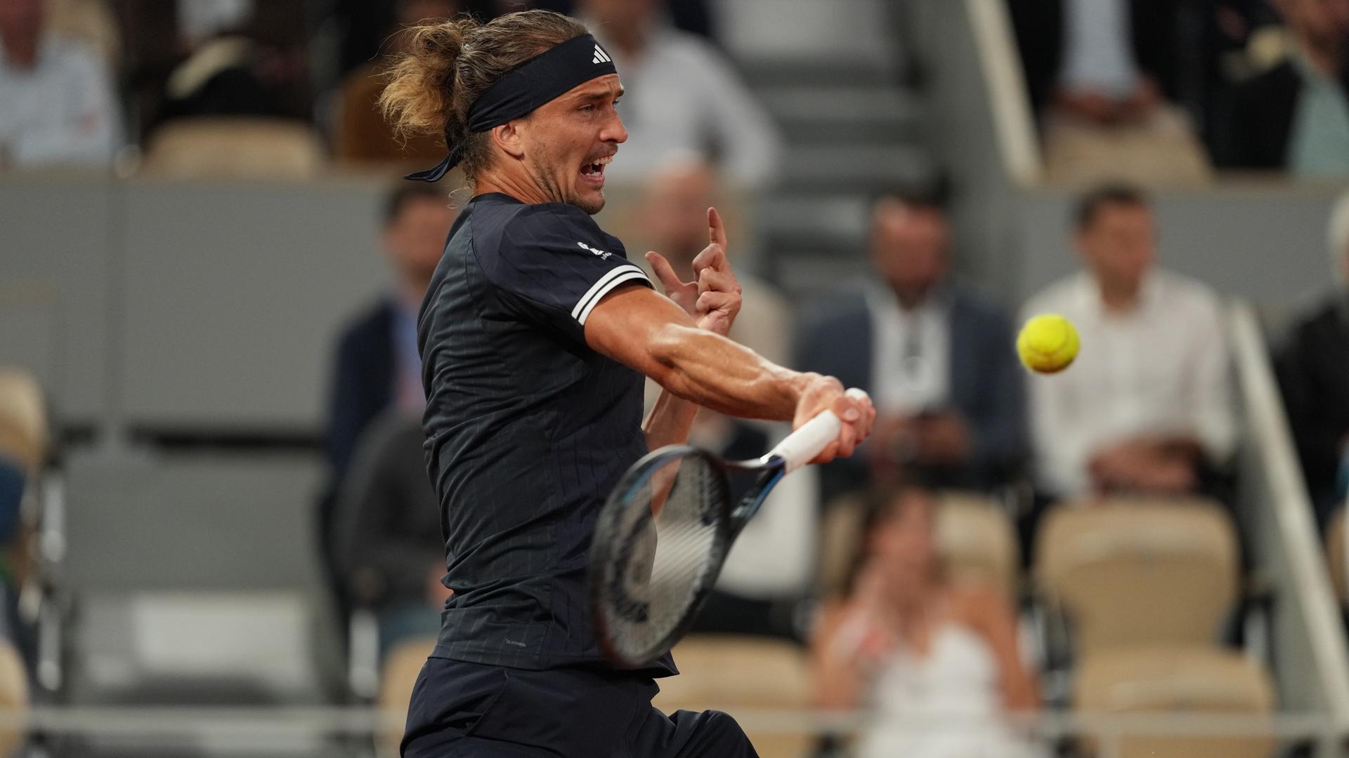 Zverev im dunklen Shirrt holt mit verzerrtem Gesicht zu einer Vorhand aus. Dahinter unscharf Zuschauer auf eine Tribüne. Zverev im dunklen Shirrt holt mit verzerrtem Gesicht zu einer Vorhand aus. Dahinter unscharf Zuschauer auf eine Tribüne.