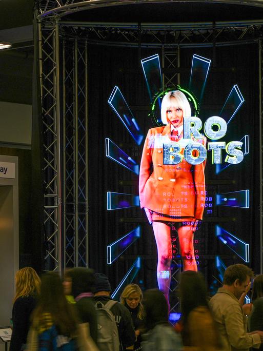 Auf einem Display auf dem South-by-Southwest-Festival in Austin ist die graphische Darstellung einer Frau zu sehen, vor ihr steht das Wort "Robots" geschrieben. 