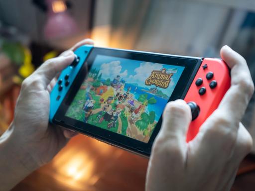 Hände halten eine Nintendo Switch und spielen darauf das Spiel "Animal Crossing"