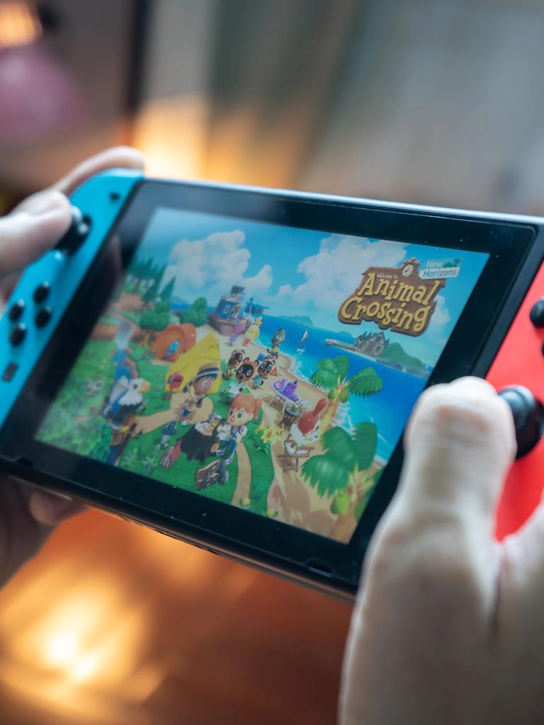 Hände halten eine Nintendo Switch und spielen darauf das Spiel "Animal Crossing"