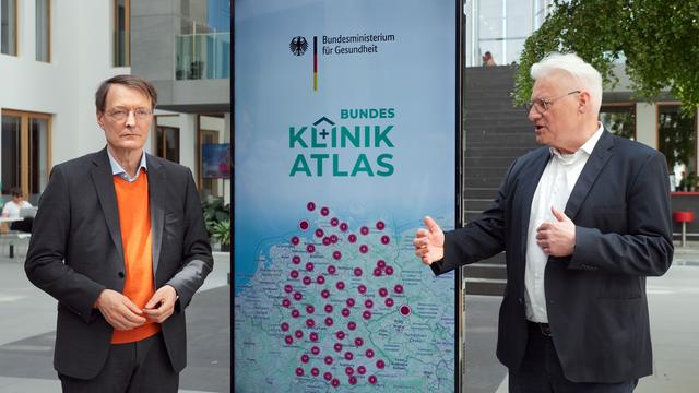 Karl Lauterbach (l, SPD), Bundesminister für Gesundheit, und Claus-Dieter Heidecke, Leiter des Instituts für Qualitätssicherung und Transparenz im Gesundheitswesen (IQTIG), stellen den Bundes-Klinik-Atlas vor. Sie stehen dabei vor einem Plakat mit dem entsprechenden Logo.