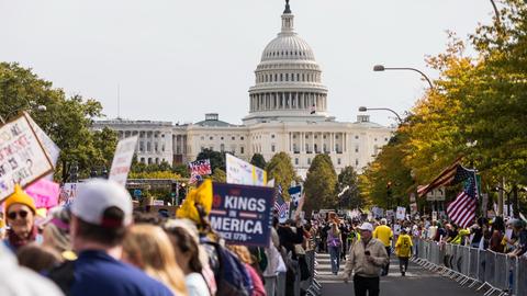 Demonstranten auf einer Straße in Washington D.C. Viele halten Transparente hoch. Im Hintergrund ist das Kapitol.