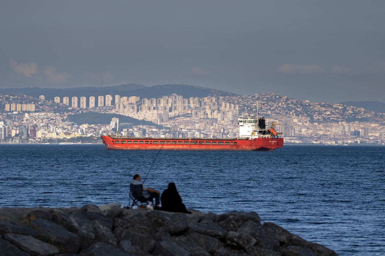 Türkei, Istanbul: Ein Frachter liegt im Marmarameer vor Anker, während Personen im Vordergrund auf einem Felsen angeln. 