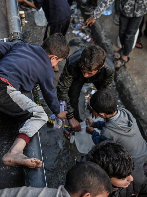 Palästinensische Kinder füllen Flaschen mit Wasser, das von Wohltätigkeitsorganisationen verteilt wurde, da der Zugang zu sauberem Wasser aufgrund der anhaltenden israelischen Blockade in Rafah immer schwieriger wird.