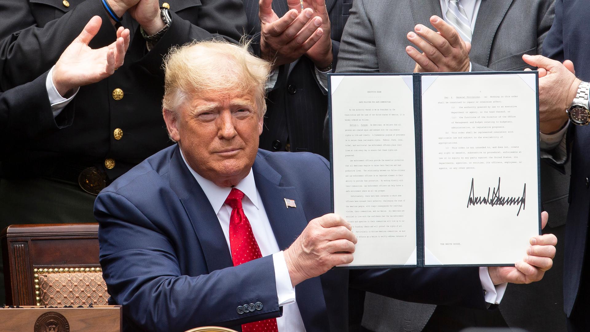 Donald Trump hält ein unterzeichnetes Buch mit einem Dekret in der Hand.