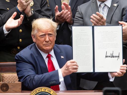 Donald Trump hält ein unterzeichnetes Buch mit einem Dekret in der Hand.