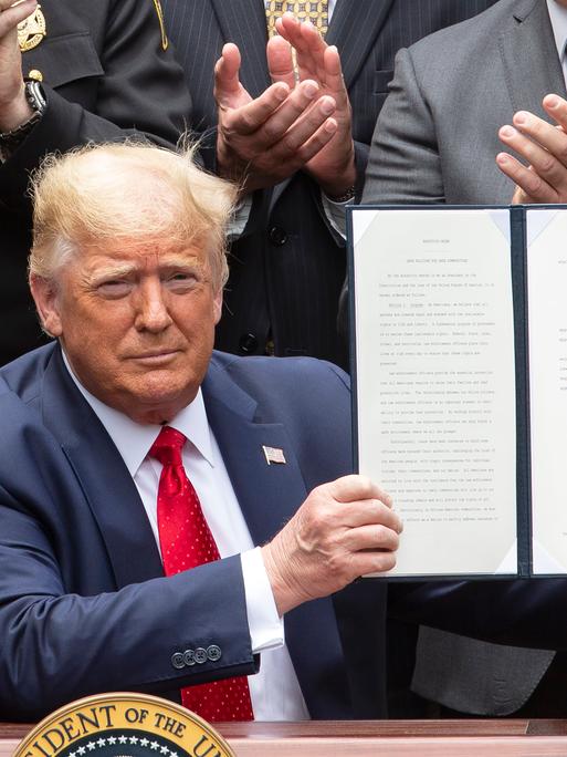 Donald Trump hält ein unterzeichnetes Buch mit einem Dekret in der Hand.